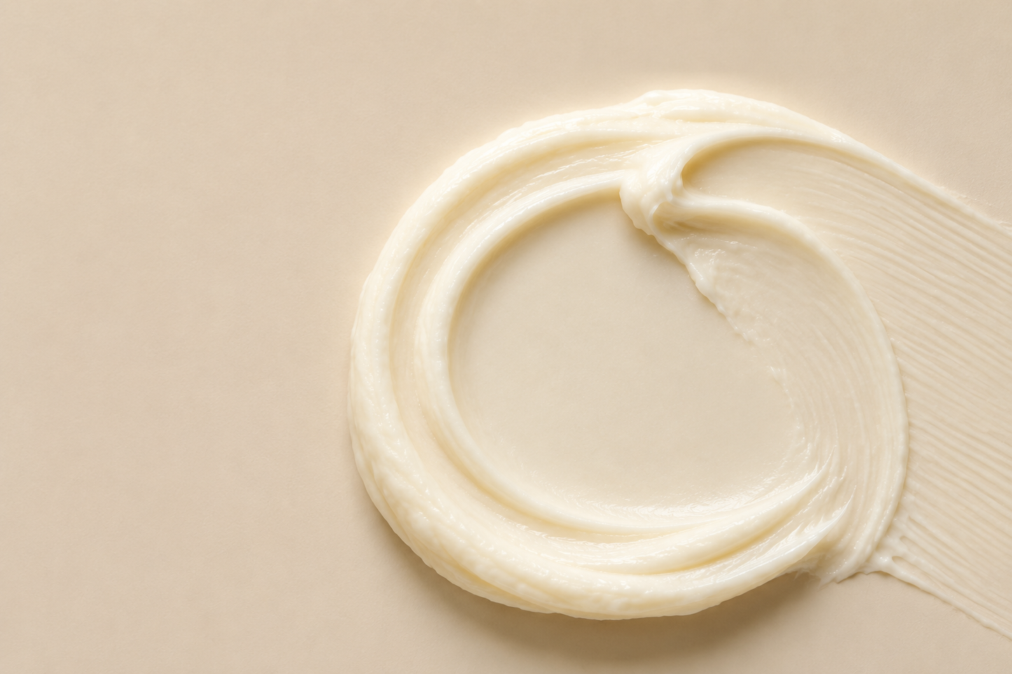 A swirl of thick, creamy off-white cosmetic cream or lotion on a smooth, light beige background.