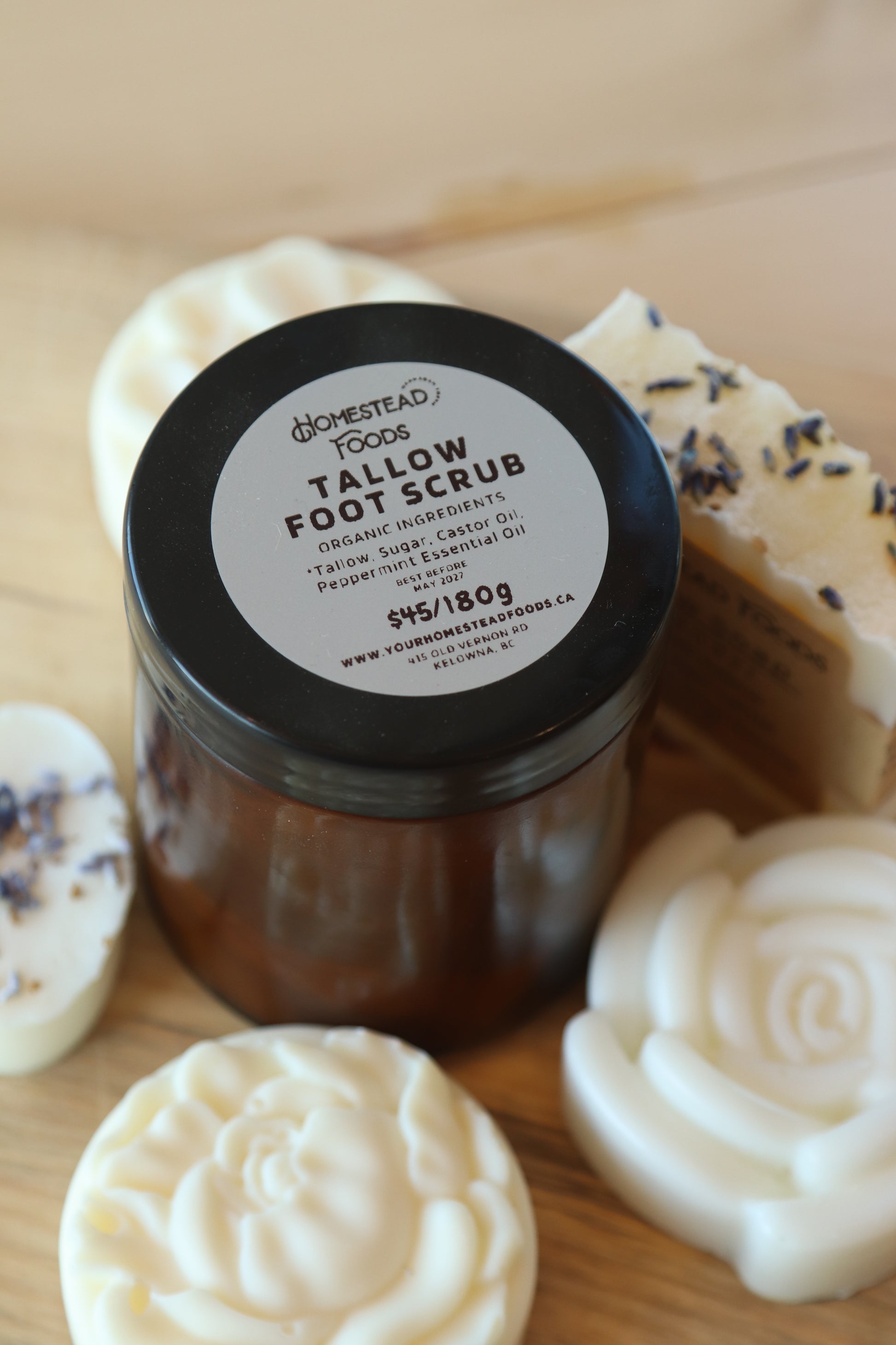 A jar of Tallow Foot Scrub from Homestead Tallow placed on a wooden surface, surrounded by tallow soap bars.