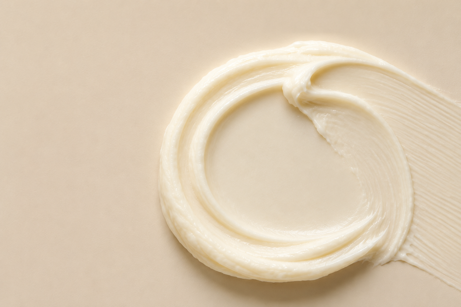 A swirl of thick, creamy off-white cosmetic cream or lotion on a smooth, light beige background.